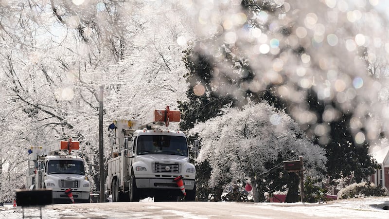 FILE: Utility trucks are seen through ice covered trees Wednesday, Jan. 28, 2026, in...